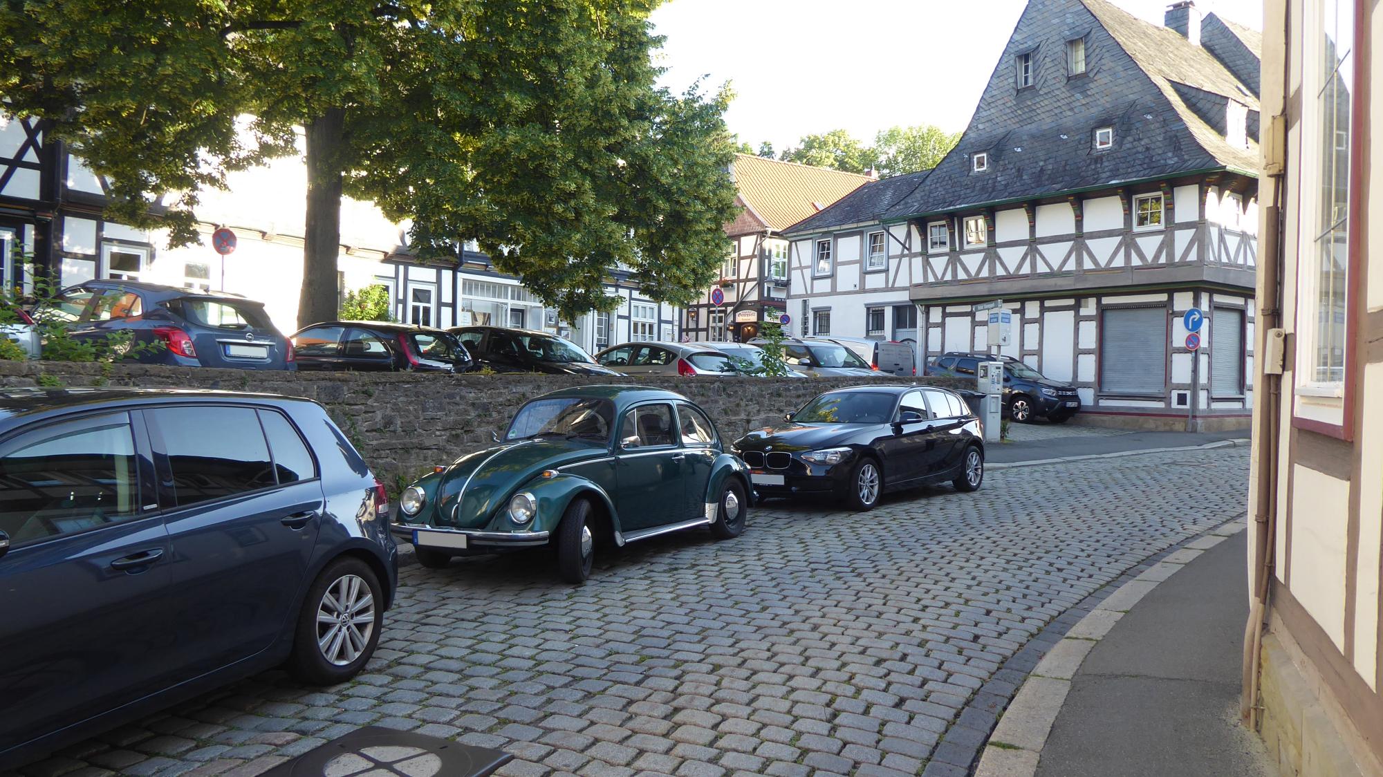Platz mit Baum. Der von Fachwerkhäsern umgeben ist. Mein Käfer ist im Vordergrund