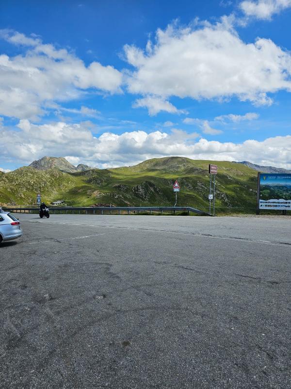 Blick vom Parkplatz, ein Motorradfahrer und Berge im Hintergrund.